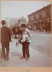 Um homem parado na calçada da Broadway entre a Rua 34 e a Rua 35, segurando o jornal The Evening Telegram