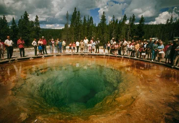 Visitantes do parque reúnem-se em torno de uma piscina termal verde-azulada em forma de flor. Parque Nacional de Yellowstone