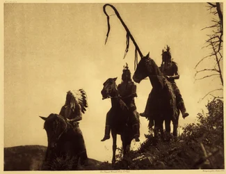 Grupo de guerra Apsaroke. O guerreiro da direita segura a vara curva de uma das organizações militares tribais. Esta vara foi plantada no chão no momento decisivo da luta, como uma faixa atrás da qual o seu portador se comprometeu a não se retirar. Foto t