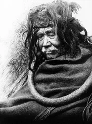 The Hamatsa, Nakoaktok c. 1910 Retrato de meio comprimento do homem Nakoaktok, virado para a esquerda, vestindo um laço cerimonial de raiz de cedro.