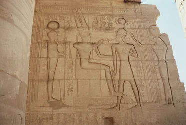 Relevo retratando a deusa de cabeça de leão Mut apresentando Ramsés II a um Amon entronizado, que lhe dá um ankh, do Grande Salão Hipostilo, Novo Reino