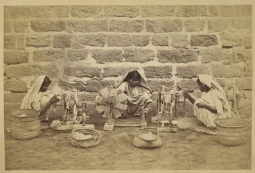 Prisioneiros femininos enrolando algodão sobre rodas de fiação na prisão de Karachi. Fotógrafa: Michie and Company c. 1873173 mm x 260 mm Archaeological Survey of India Collections: Série Escritório da Índia (Volume 52).