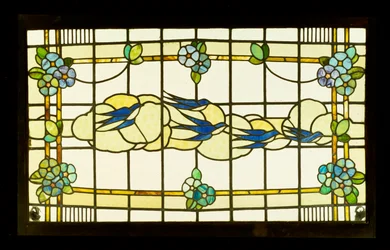 Painel de artes e ofícios de um grupo de andorinhas diante das nuvens em uma borda de cabeças de flores estilizadas (vitrais com chumbo)
