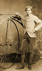 Homem de pé junto à sua bicicleta de roda alta, cerca de 1890