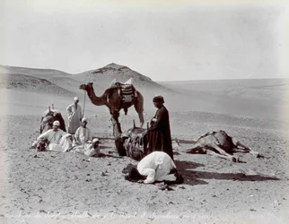 Cameleiros egípcios durante uma pausa no deserto. Em primeiro plano, dois membros do pequeno grupo parecem estar rezando