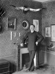 Retrato de um jovem, posando na sala de estar decorando a Abadia de Septfontaines, perto de Bourmont en Haute Marne. Fotografia de finais do século XIX. Coleção Ducos.