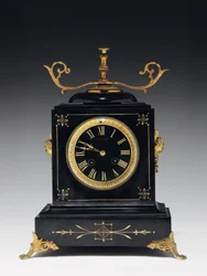 Relógio de manto em pedra preta de composição, com decoração incisa, com pés, remates e ferragens em latão dourado, de Jausions de Pau, França, c.1876-78