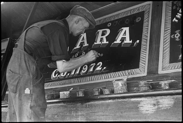 Frank Jones, a trabalhar na pintura do painel de nomes de uma barcaça, século XX (foto)