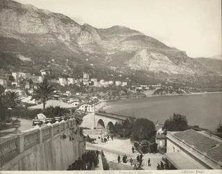 Vista panorâmica de Montecarlo no Mónaco. A cena mostra vários transeuntes; à esquerda vemos um grande plano de uma balaustrada de mármore.