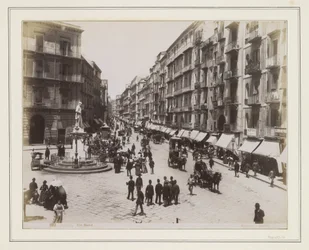 Vista da Via Roma em Nápoles com uma estátua, lojas, carruagens puxadas por cavalos e transeuntes
