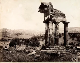 Vista das quatro colunas restantes que suportam uma entablatura do Templo de Castor e Pollux no Valle dei Templi, Agrigento. Um panorama da cidade é visível em segundo plano.