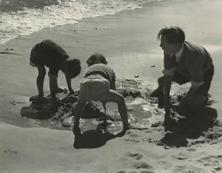 Três crianças a brincar com areia na praia.