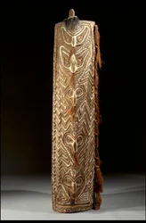 Escudo Sepik retangular curvo, a frente com faixa central de cinco máscaras, cada uma com fibra no septo perfurado, dentro do painel de ziguezagues esculpidos (madeira, penas e ráfia)