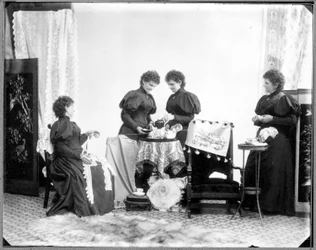 Exposição múltipla de Hannah Maynard - duas a tomar chá, uma segura uma meada de algodão, uma enrola-a numa bola, c. 1895