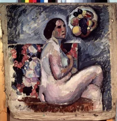 Akt. Retrato de uma mulher nua, sentada de pernas cruzadas, de perfil, fazendo um gesto de modéstia. Atrás dela, um quadro de fruta e um chapéu decorado com fruta pendurado na parede. Pintura de Ilya Ivanovich Mashkov (Ilia Machkov, Matchkov) (1881-1944)