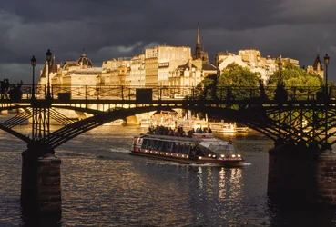 Nuvens negras sobrevoam o céu enquanto um barco passa sob a Pont des Arts. Rio Sena, Pa...
