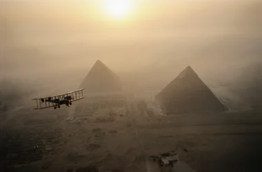 O avião Vimy voa sobre as pirâmides envoltas em nevoeiro durante um dia de sol dourado...