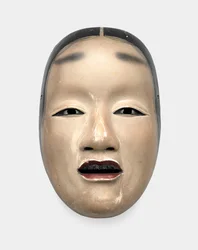 Uma máscara de madeira com fundo de gofun, pintada com sumi para os cabelos, olhos e dentes e vermelha para os lábios