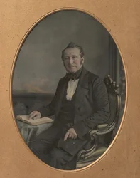 Homem sentado apontando para uma passagem em um livro aberto, década de 1850.