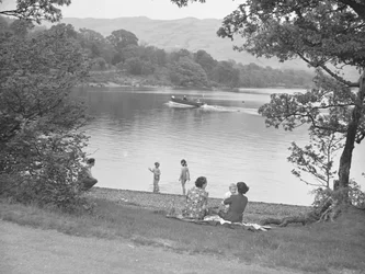 Uma família diverte-se junto a um lago, com um barco no lago e as montanhas ao fundo