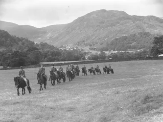 Um grupo de homens em fila, montados em póneis, com as montanhas ao fundo