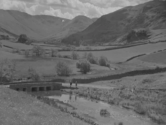 Vista de uma ponte, de um riacho, de campos e de montanhas