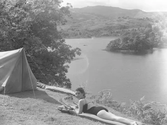 Vista de uma jovem mulher com um fato de banho e deitada num lilo, com um lago ao fundo