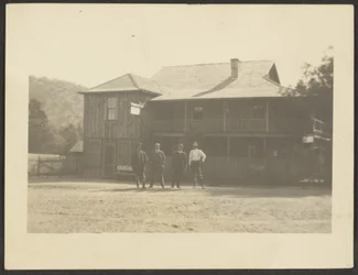 [Quatro homens diante de um edifício de madeira].