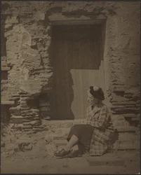 [Mulher sentada diante de um edifício em degradação]