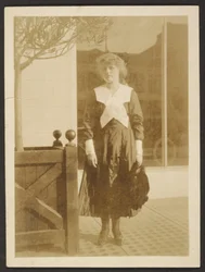 [Mulher de pé na calçada].