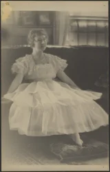 [Mulher com vestido de chiffon sentada num sofá]