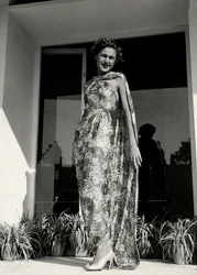 Modelo veste um vestido comprido com um padrão floral criado pela casa de alta costura "Graldi". O artigo é complementado por um manto do mesmo tecido. (foto a p/b)