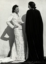 Dois modelos apresentam criações da casa de alta costura italiana "Dragoni". Um modelo veste uma roupa em material fralda composta por uma jaqueta e saia comprida com trem. O outro modelo, visto de trás, veste um longo manto de veludo. (foto a p/b)