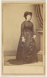 [Mulher não identificada com chapéu e vestido comprido escuro.]