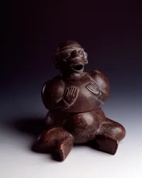 Arte pré-colombiana, civilização maia, período inicial: vaso antropomórfico de barro representando um homem sentado, com as mãos sobre o peito, usando uma máscara de macaco de boca aberta. Proveniente de Uaxactún, Guatemala. Dimensões: alt. 22,5 x larg.