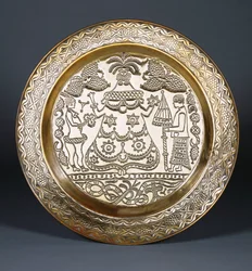 Um carregador de latão Efik em relevo com uma figura feminina vestida no centro e dois servos segurando um leque e um guarda-chuva