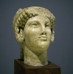Cabeça de menina (Kore), escultura do período helenístico romano (3o século 2 depois da nossa era), rosto muito expressivo, maçãs do rosto proeminentes a leste, sorriso, cabelo encaracolado, estilo arcaico de Ionie no século 6 antes da nossa era que se per