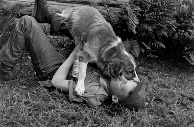 Um jovem brinca com o seu cão no exterior da sua cabana de madeira em Palmer, Alasca