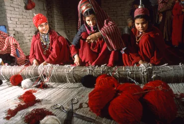 Mulheres de tribos turcomanas tecelãs cortam os nós da urdidura de um tapete num tear na aldeia de...