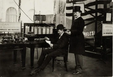 Lee DeForest (sentado) enviando uma mensagem telefônica sem fio no Departamento de Eletricidade na Feira Mundial de 1904
