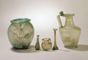 Colecção de vidro romano: urna cinerária, vidraria funerária e jarro, séculos I-IV