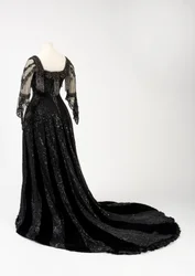 Vestido de noite preto comprido usado pela rainha Alexandra, com decoração de missangas e lantejoulas e incorporando a característica fita de seda preta da rainha Alexandra com o nome em letras douradas, feito por Barolet of Knightsbridge, Londres