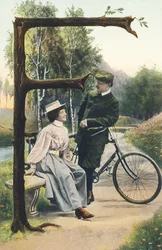 F: Um homem vestido de ciclista e apoiado na sua bicicleta está falando com uma mulher sentada num banco. Decoração do campo - Alfabeto caracteres Ref Th. E., L. Theochrom - Serie 994. Theodor Eisman, editor, Leipzig