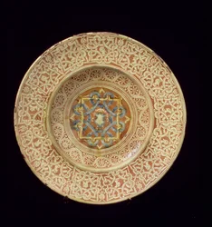 Placa Maiolica decorada com um elaborado desenho de nó repetitivo emoldurando cabeças de perfil na borda e um escudo na placa central, italiana, feita na Toscana