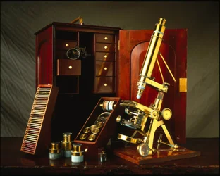 O microscópio de soutiens Powell e Lealand tem três pernas equipadas com uma caixa de madeira com vários acessórios.