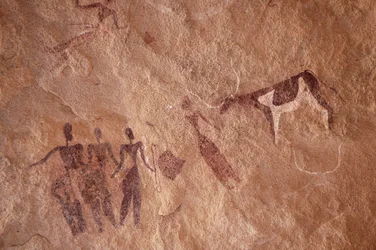 Arte rupestre, Pré-história: Pintura rupestre de um grupo de personagens e uma vaca de duas cores com chifres grandes num abrigo ornamentado, no maciço de Uweinat, Egipto. (Período de 8000 a 3000 anos a.C.). Fotografia