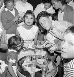A ATRIZ E MODELO ELSA MARTINELLI NO XVIII FESTIVAL INTERNACIONAL DE CINEMA NO LIDO DE VENEZA (dá autógrafos a jovens admiradores. Sobre a mesa está uma garrafa de Schweppes) - 1957