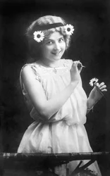 Mulher a tirar pétalas de uma flor: "Ele ama-me. Ele não gosta de mim. Ele ama-me..." Fotografia por volta de 1912