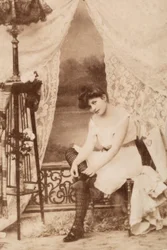 Retrato de uma jovem mulher em trajes íntimos, sentada enquanto ata o seu sapato.