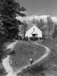 Os homens reuniram-se à porta de um pequeno edifício rural, de uma escola ou de uma igreja com sino...